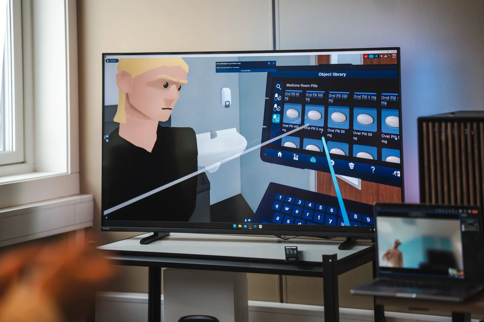 Bjørn Morten fra Fynd Reality instruerer oss i Medisinrom VR. Han skimtes i real life på Teams, og virtuelt på tv-skjermen. 🤯